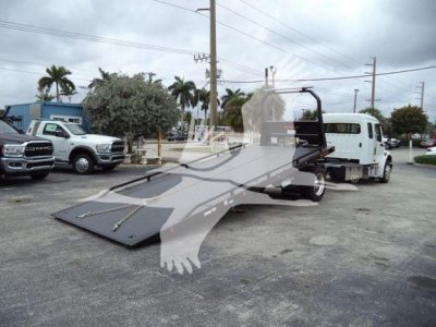 Freightliner M2 106 rollback truck with lowered flatbed in a dealership lot.