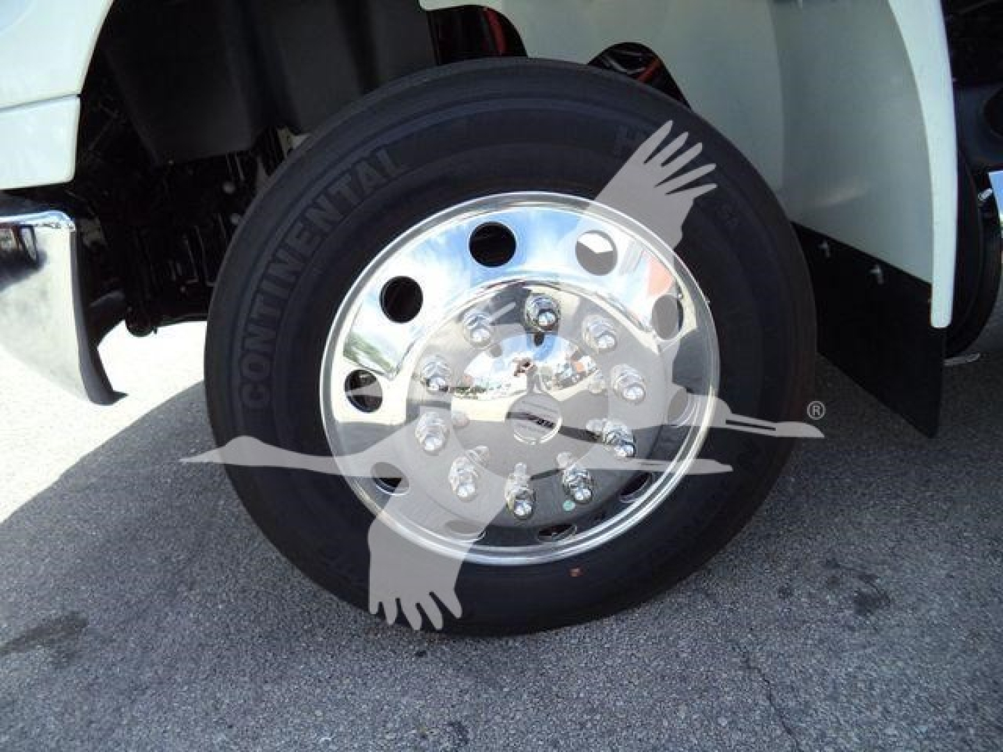 Truck wheel with Continental tire and shiny aluminum hubcap; part of a white truck fender visible; watermark with two crossed hands.