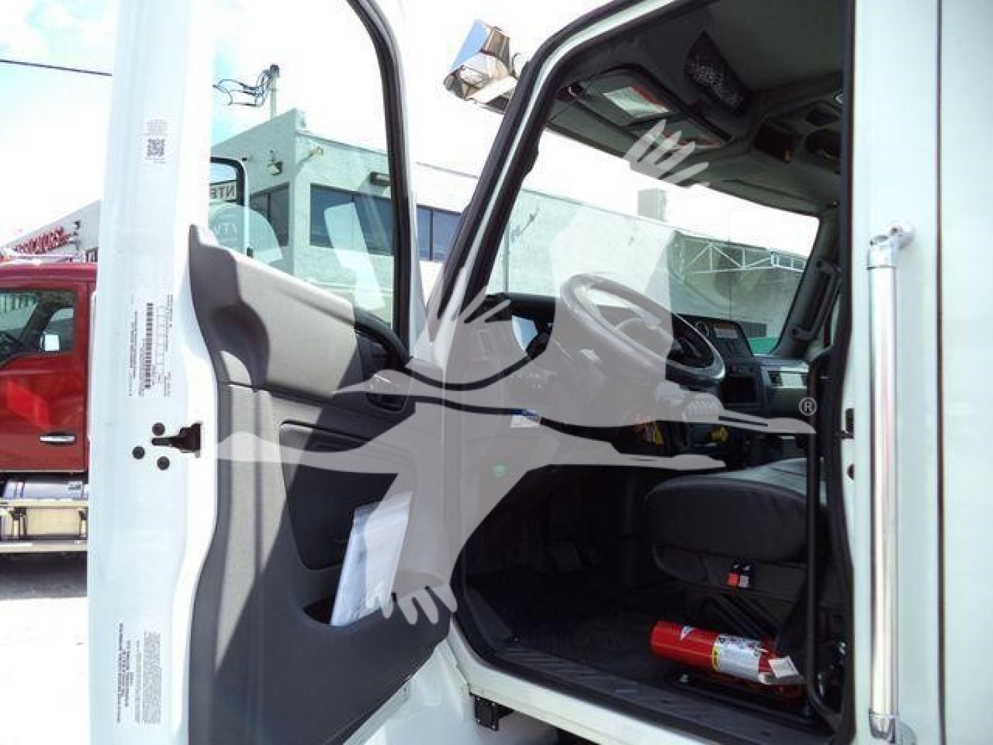 Truck cab interior of a 2026 International MV in the open door, showing steering wheel, dashboard, and driver seat.