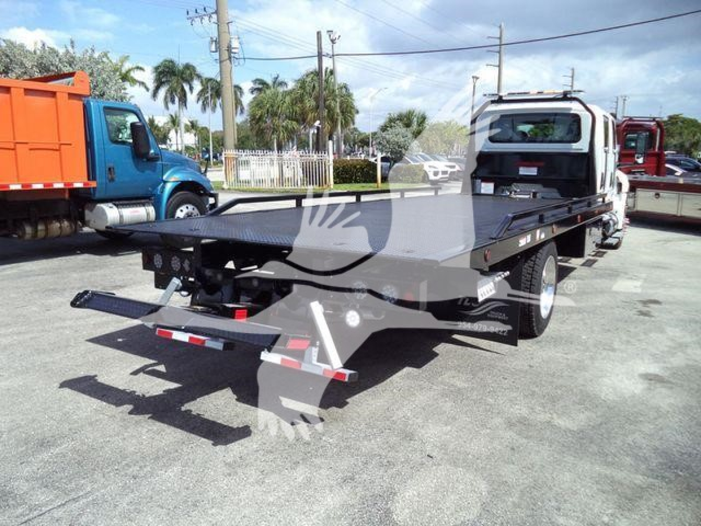 International MV rollback truck flatbed showing steel flatbed, rear bumper, and towing hitch with wheel lift apparatus.