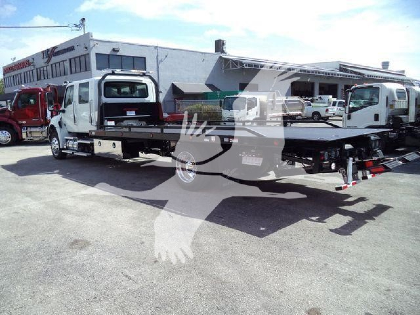 MV International truck flatbed rollback with crane arms and cab in a dealership lot.