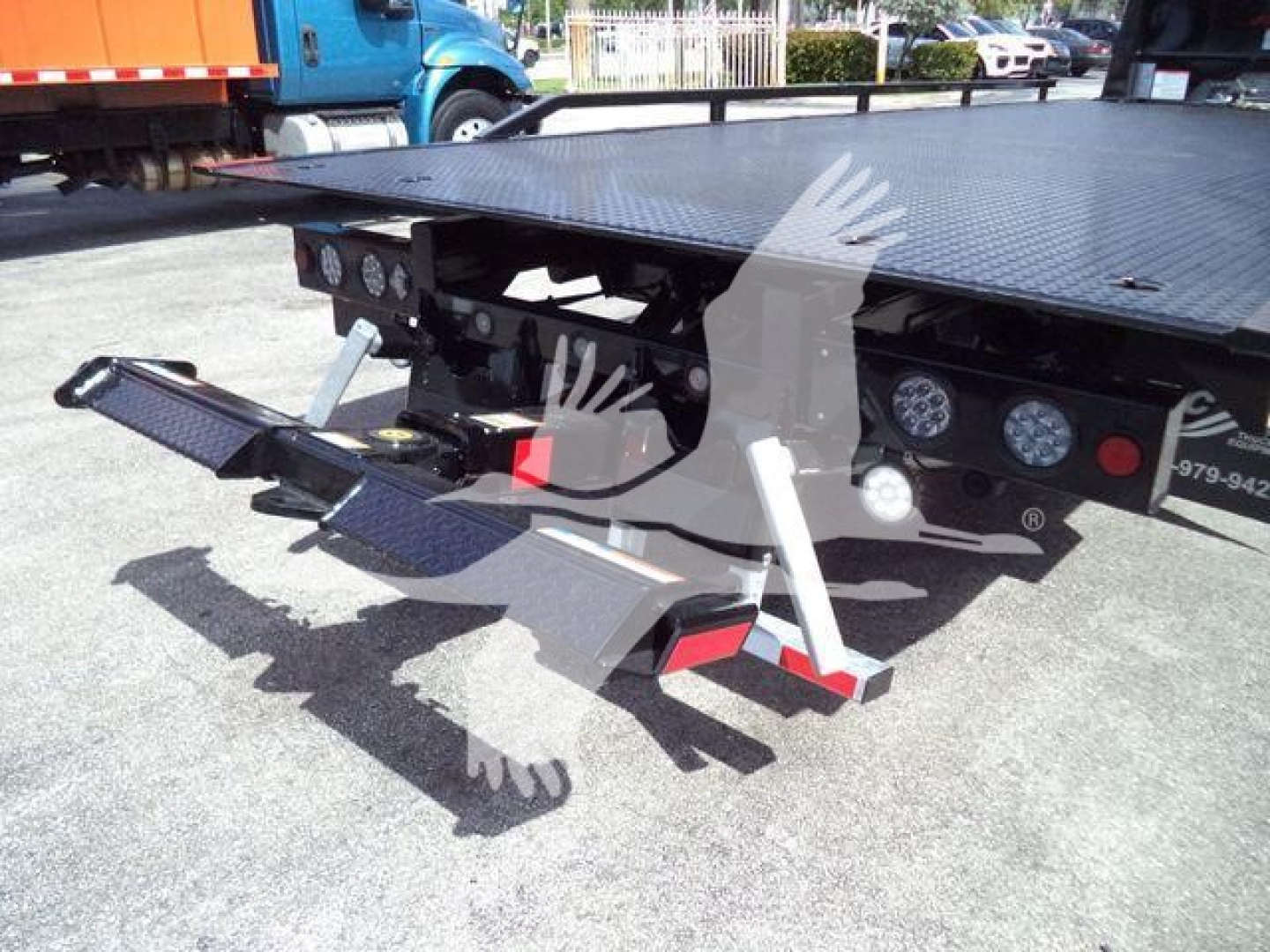 Flatbed rollback truck bed with hydraulic controls and wheel ramps visible, International MV model in the background.