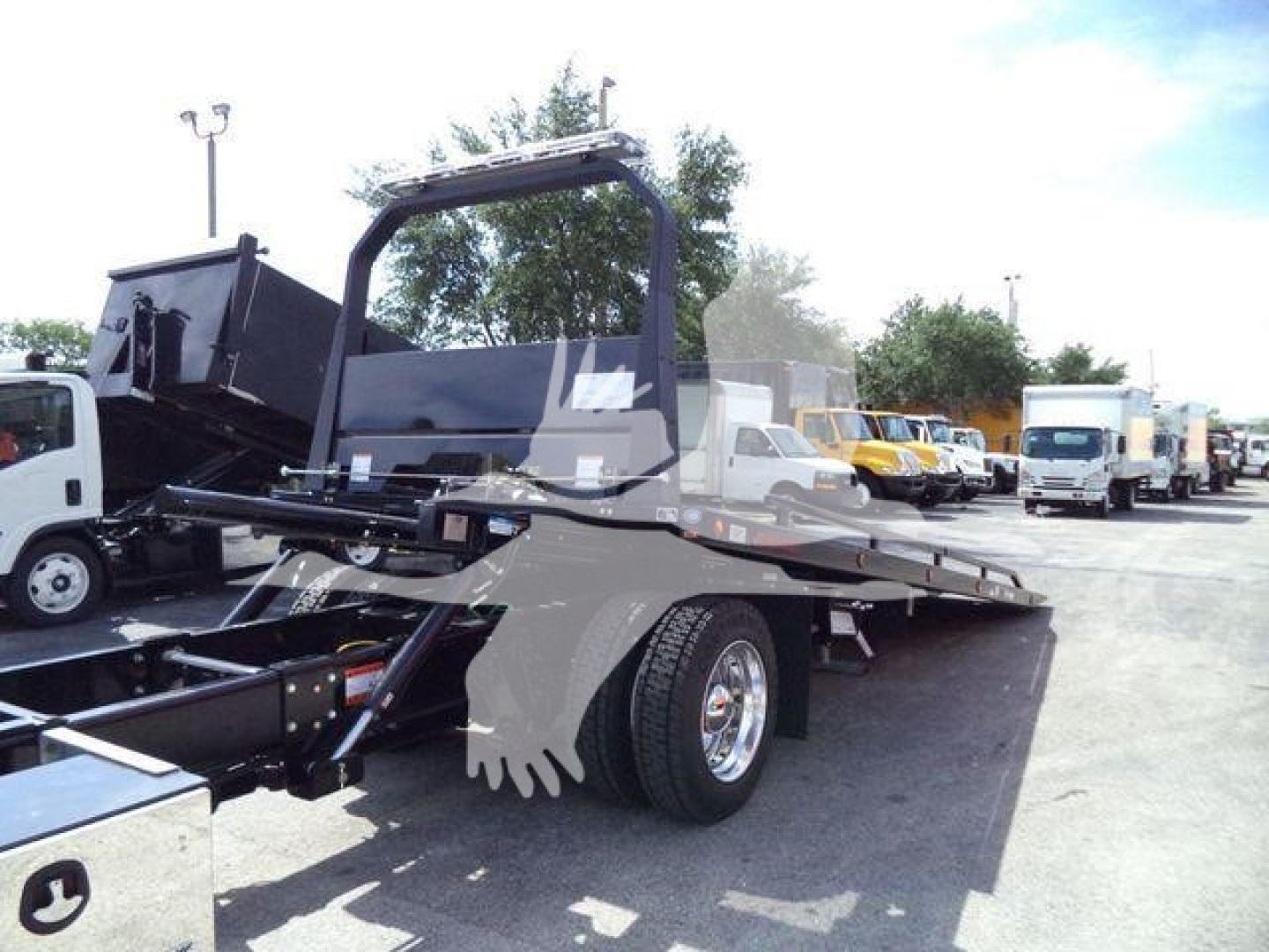 Truck flatbed tow area with hydraulic bed and rear wheels visible; other trucks in lot in background