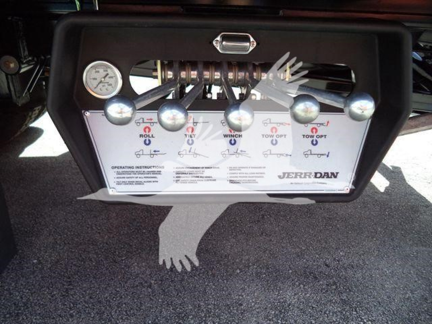Panel with multiple control levers and a gauge on a truck rollback unit, labeled switches for roll, winch, and tow operations, mounted on a black frame.