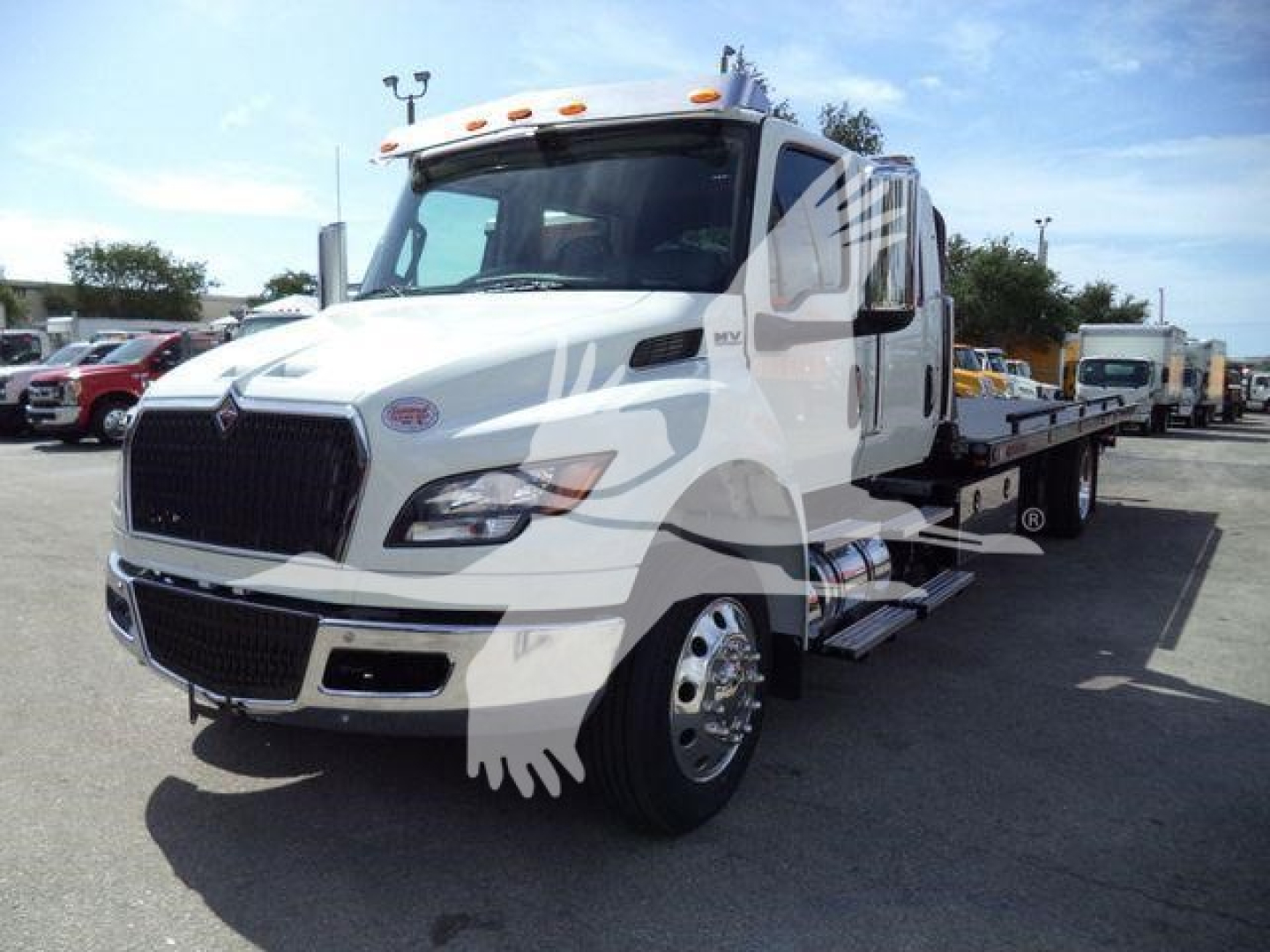 Truck cab showing International MV model with front grille and side mirrors; Rollover tow truck with car hauler bed in a dealership lot.