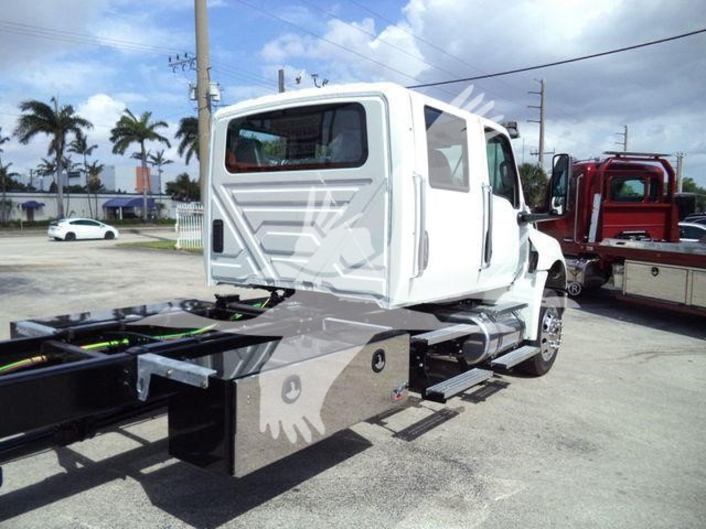 Truck chassis and cab of a white 2026 International MV roll-back truck showing side view with metal toolbox and hitch area.