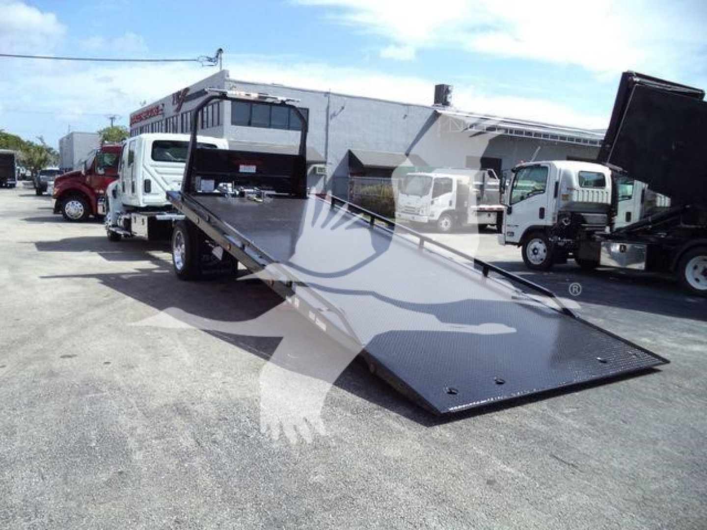 Truck with a lowered flatbed ramp in a dealership lot, International MV model, rollback truck, rear ramp extended for loading.