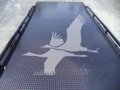 Flatbed/ramp with a large white gull logo on dark textured surface; industrial truck equipment part with raised edges along sides.