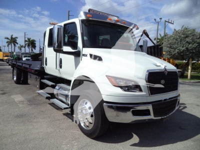 White 2026 International MV rollback truck front left view showing cab and flatbed trailer in a dealership lot.