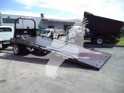 Flatbed rollback truck with lowered deck and loading ramps in an outdoor lot.