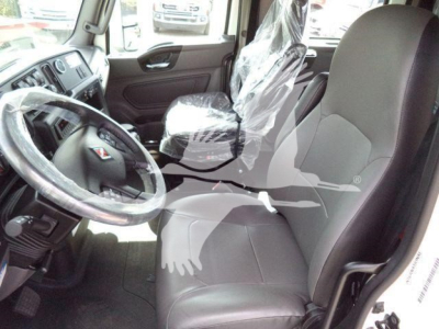 Truck cab interior showing driver's seat with protective plastic, steering wheel, and front passenger seat; plastic-wrapped seat material and dashboard visible.