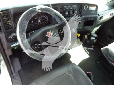 Interior of a truck cab showing steering wheel and dashboard with plastic cover over wheel and gear selector area.