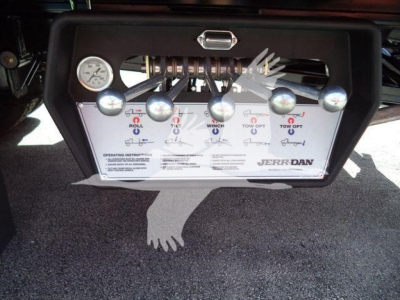Panel with multiple control levers and a gauge on a truck rollback unit, labeled switches for roll, winch, and tow operations, mounted on a black frame.