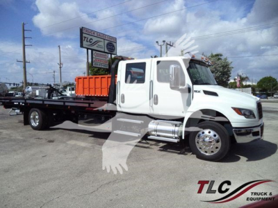 International MV tow truck chassis with rollback bed, white cab, orange loading bed accessories, side exhaust, chrome wheels, in dealership lot.