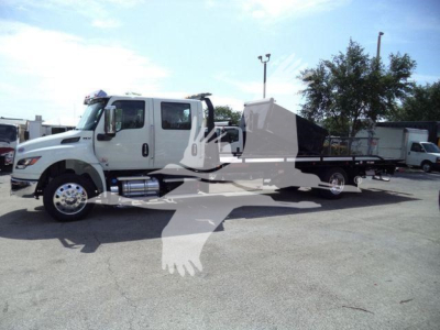 Truck with a large flatbed and dual rear axles, white cab, side mirrors, chrome fuel tank, and rollback equipment. Visible text includes no legible labels on the image.