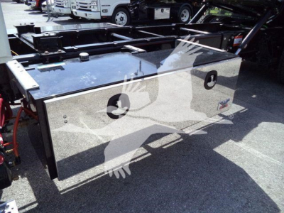 Truck toolbox mounted in flatbed area showing aluminum hinged lid with two circular pad eyes and reflective surface