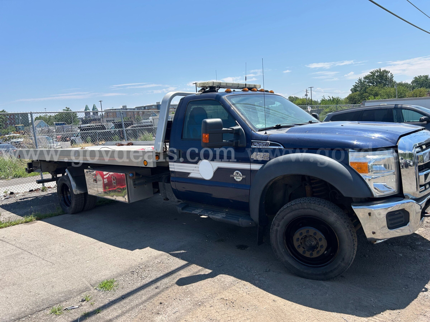 Ford F-550 flatbed truck side view showing utility toolbox and dual rear wheels.