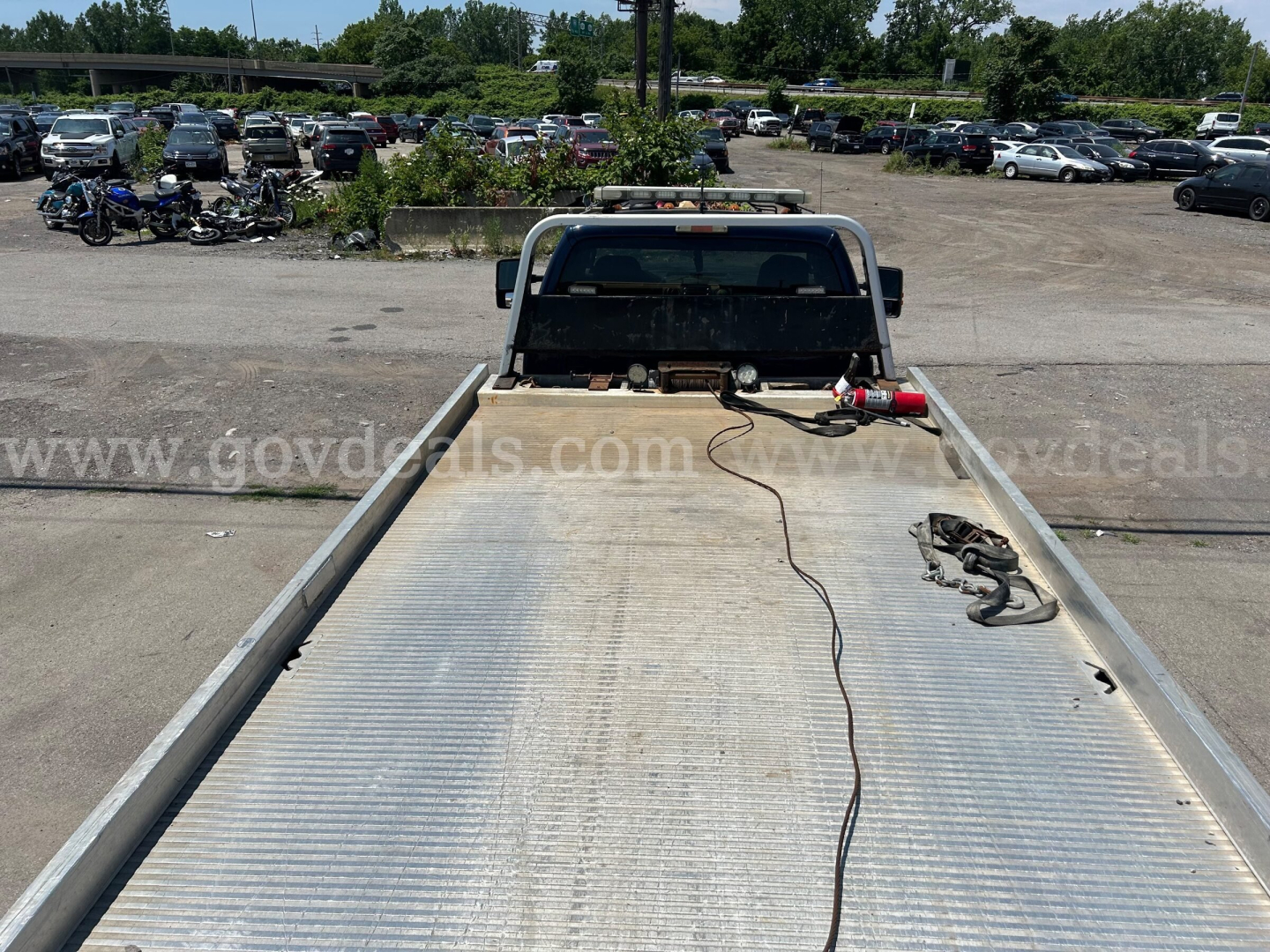 Flatbed tow truck bed with aluminum surface and tow hitch, rear view of sleeper cab and windshield, power cables and hooks on the bed.