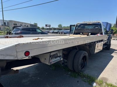 Flatbed tow truck rear/side view showing flatbed and dual rear wheels, aluminum deck, rectangular tail lights, Ford F-550 likely chassis, in-service condition.