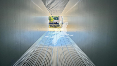 Trailer interior showing clean metallic walls and ribbed floor with loading doorway at end.