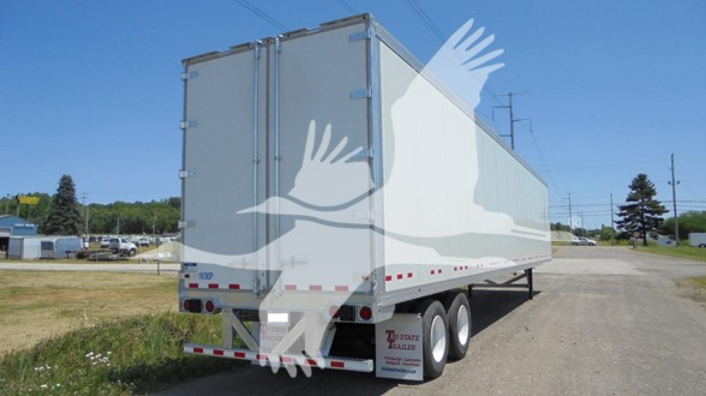 Rear and side view of a Vanguard VXP trailer with white exterior, double rear doors, and safety decals on the lower rear; no legible branding text visible.