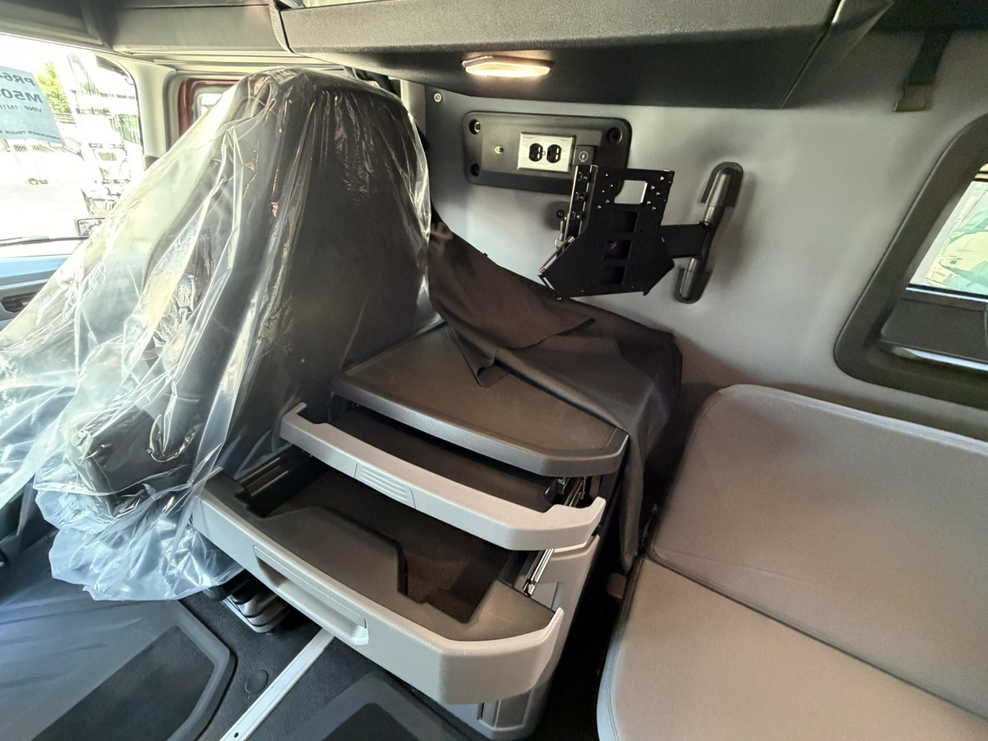 Truck interior showing driver seat with protective cover and storage drawers under a dashboard panel.