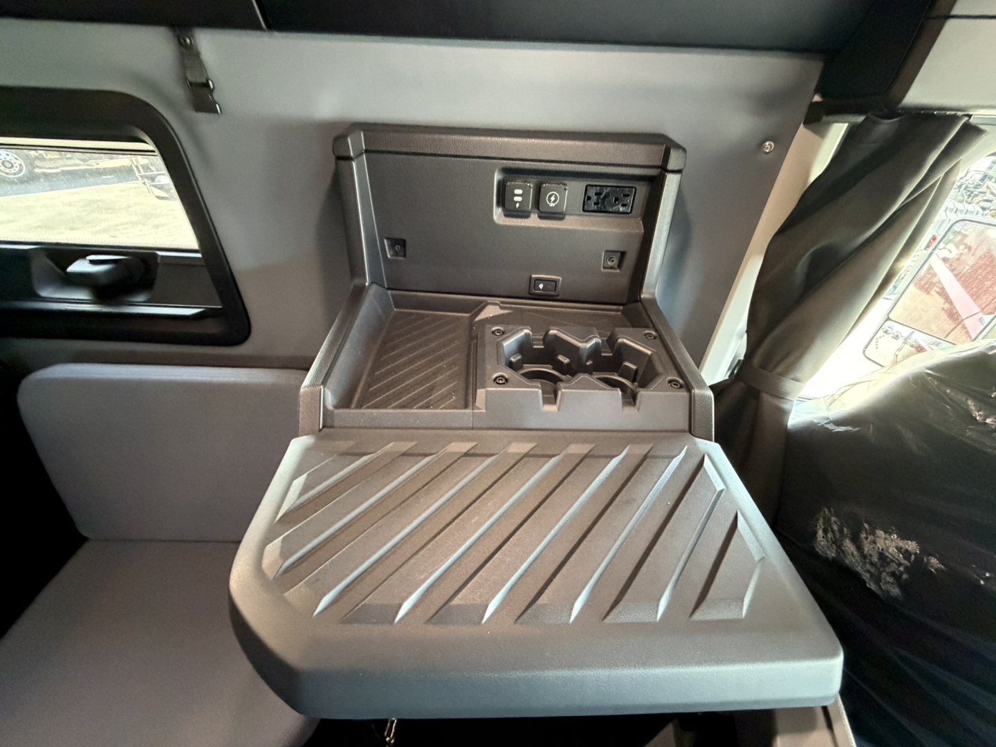 Truck interior center console with fold-out tray, cup holders, and power/USB outlets panel. Fold-down surface shows ridged texture.