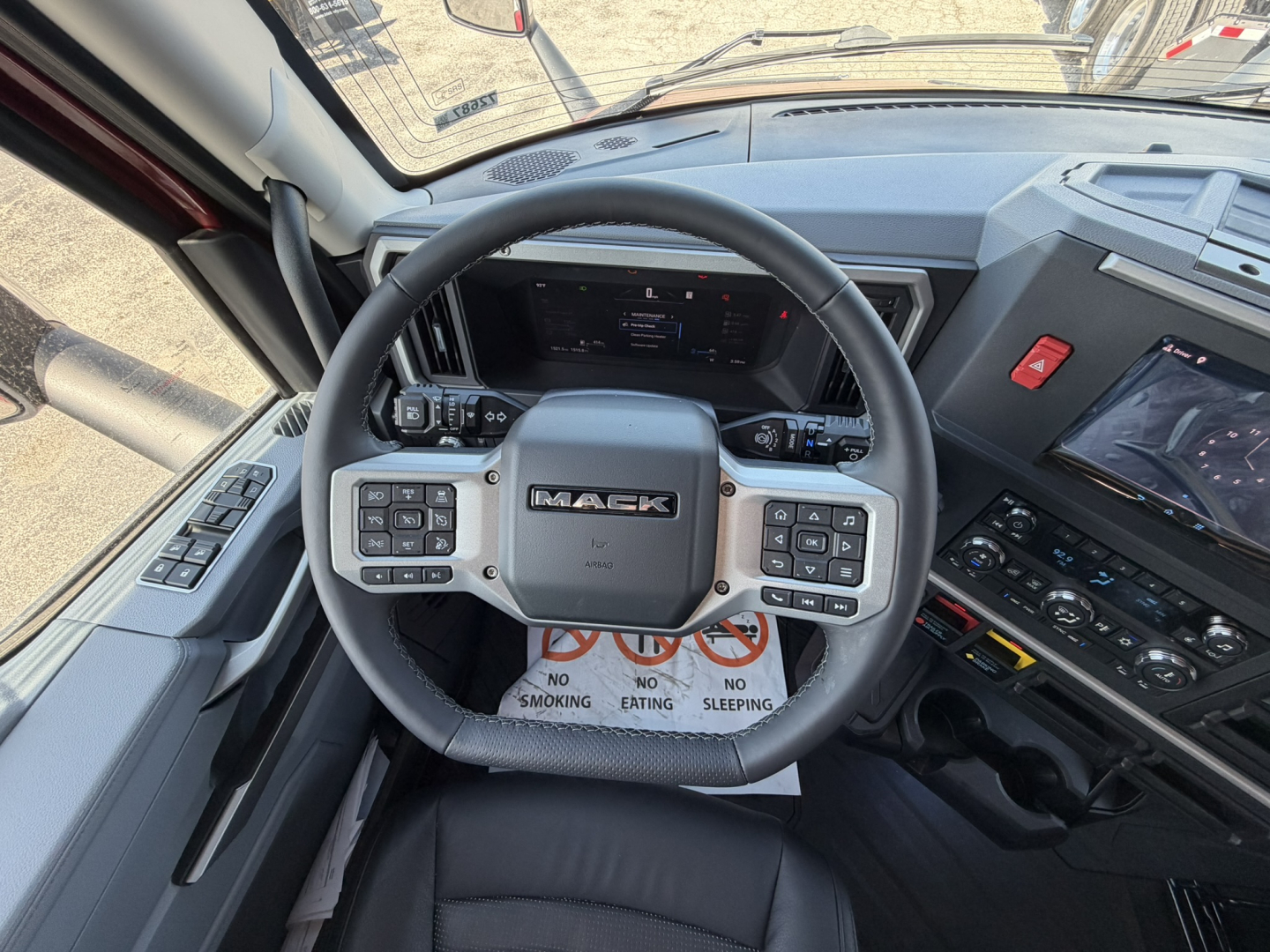 Mack PR64T76H truck interior steering wheel view with digital dash and controls visible in cab, driver seat area, no smoking sign on floor mat.