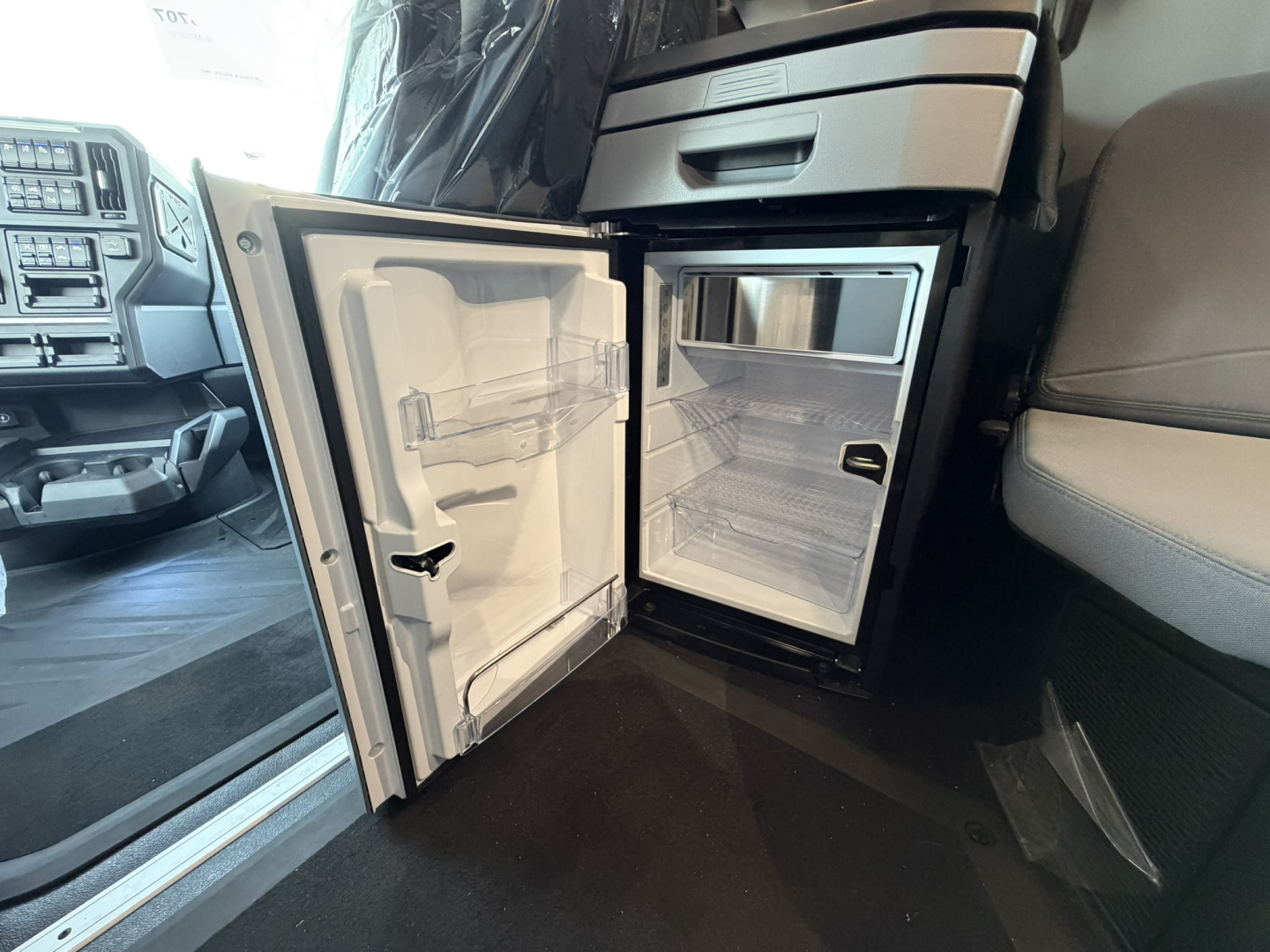 Mack PR64T76H truck interior showing open under-cab refrigerator and small freezer in a compact kitchenette area.