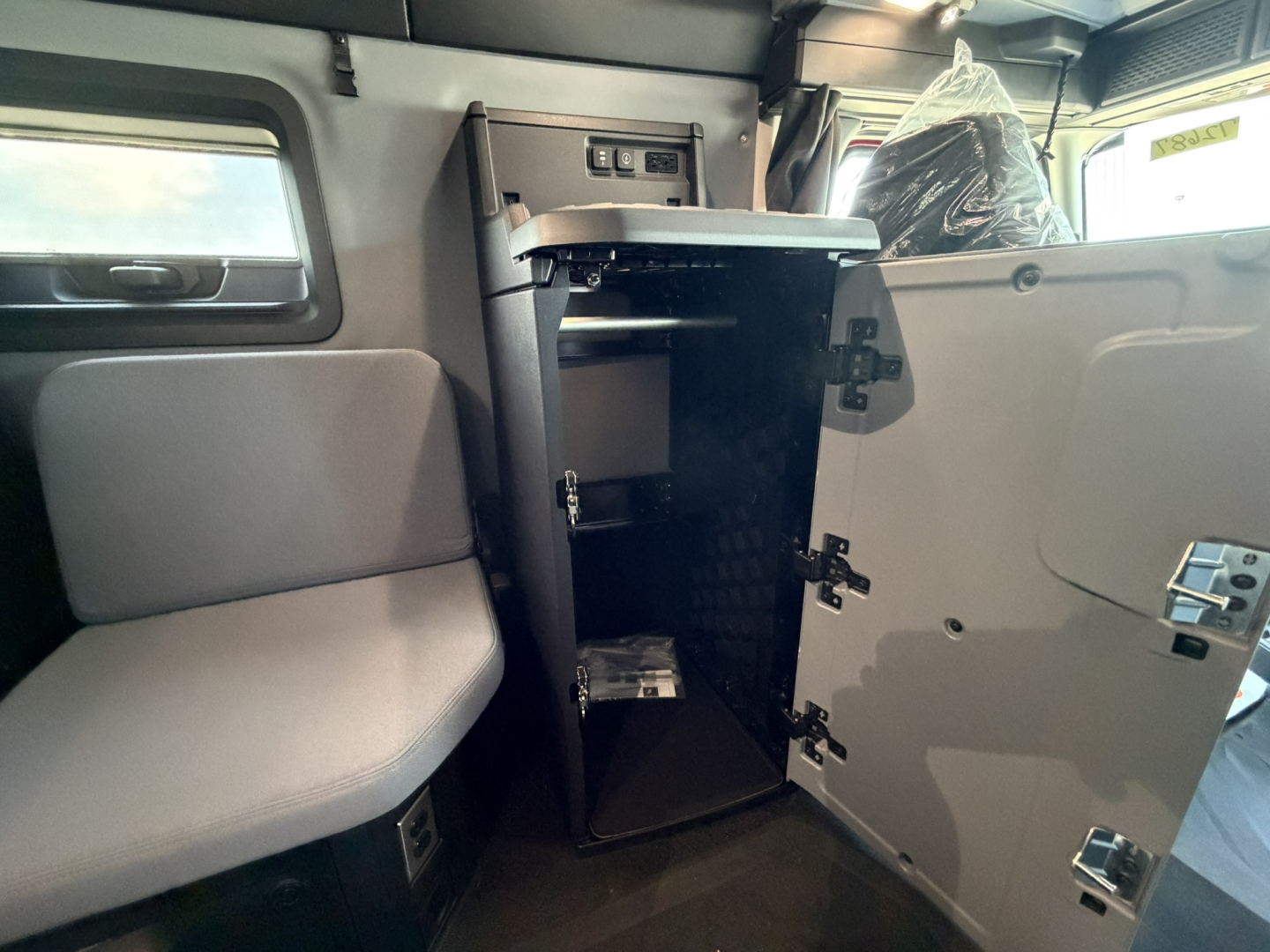 Truck cab interior with a tall open cabinet or storage locker showing shelves and a small top drawer, adjacent to a seat and door.