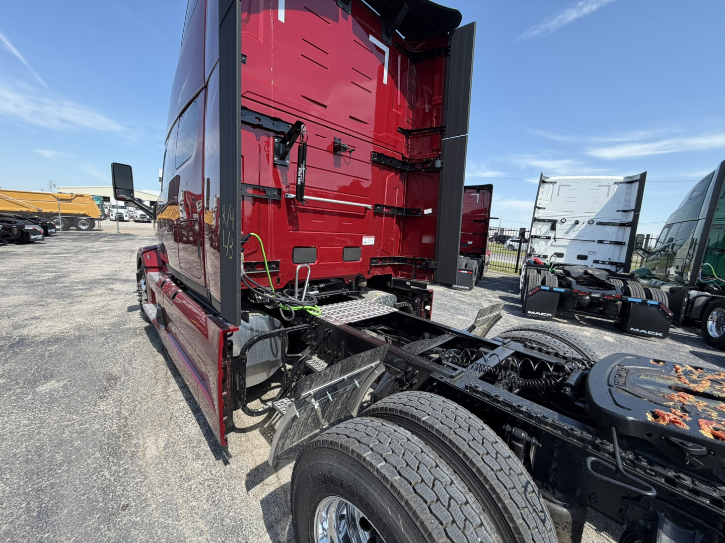 Truck cab rear view showing fifth wheel and chassis on a Mack PR64T76H conventional sleeper. Visible frame, rear wheels, and red cab with vertical doors.