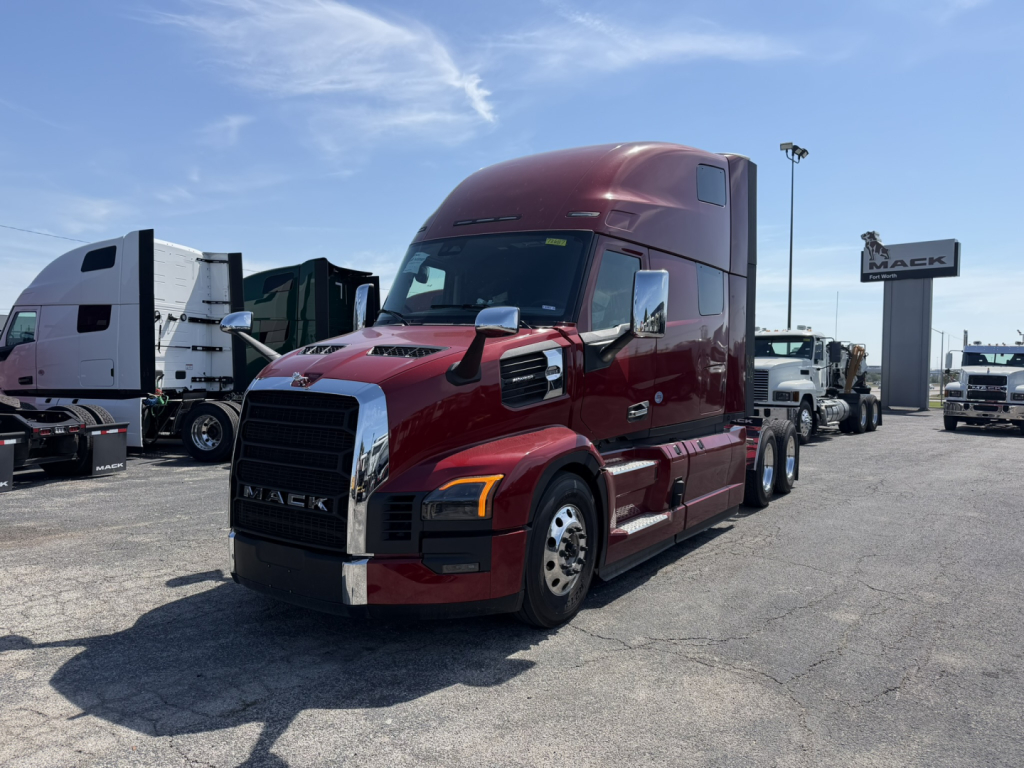 Mack PR64T76H truck in a dealership lot, burgundy color, front three-quarter view, with other trucks in background and a Mack sign.