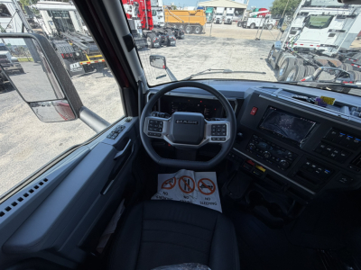 Truck cab interior showing steering wheel with Mack emblem, dashboard controls, and a warning placard on the seat area.