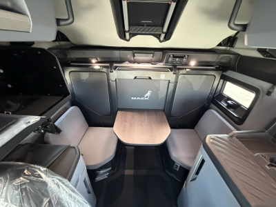 Cab interior of a new Mack PR64T76H sleeper with front seating and table, dashboard area, and overhead storage visible.