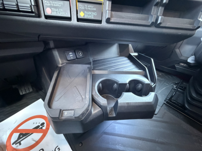 Interior of a Mack truck cab center console with cup holders, storage, and control switches. Visible text includes warning labels and icons.