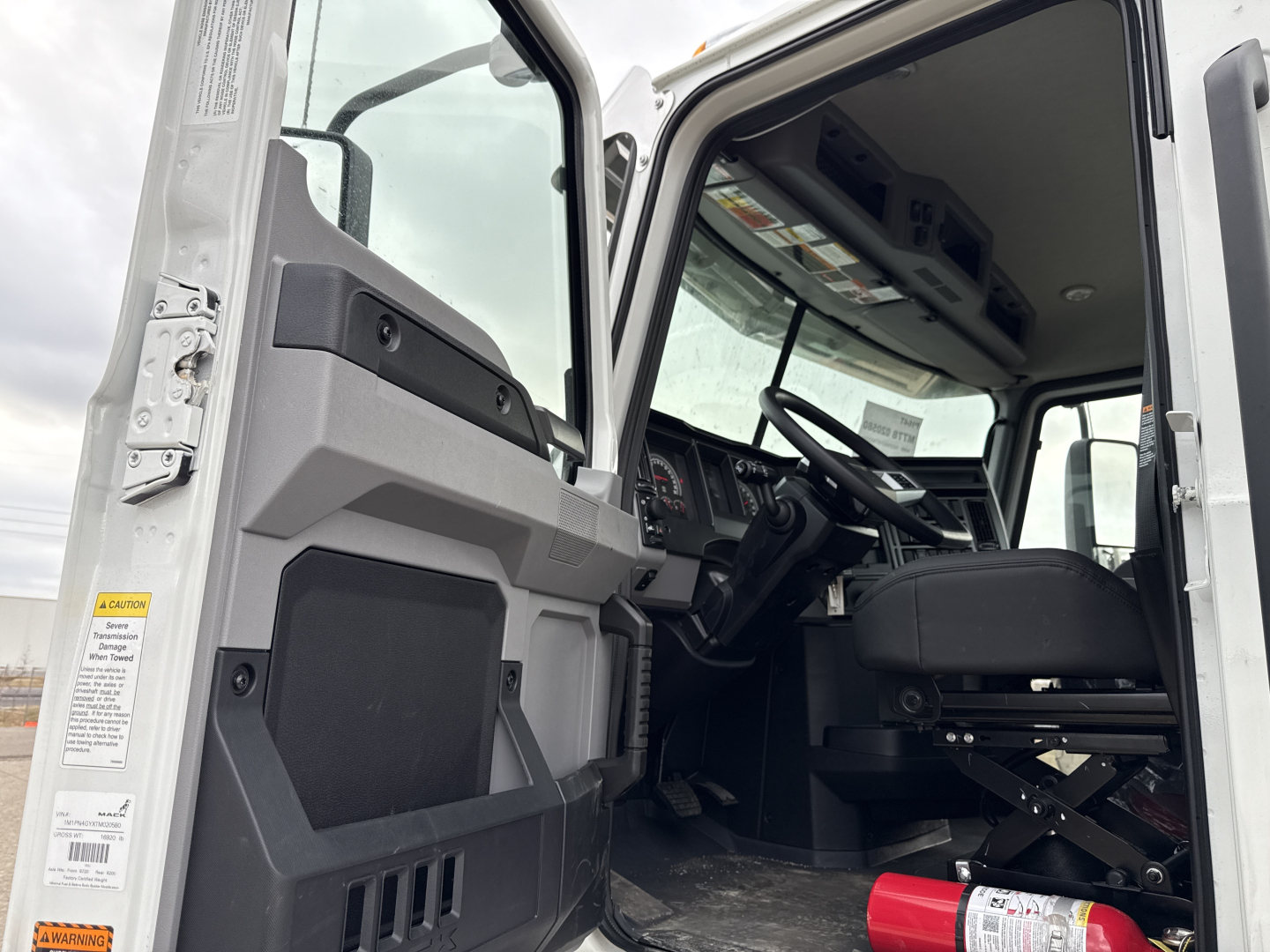 Front cab interior of 2026 Mack PI64T with open door showing steering wheel, dashboard, and driver's seat; VIN tag and spec labels on door frame.