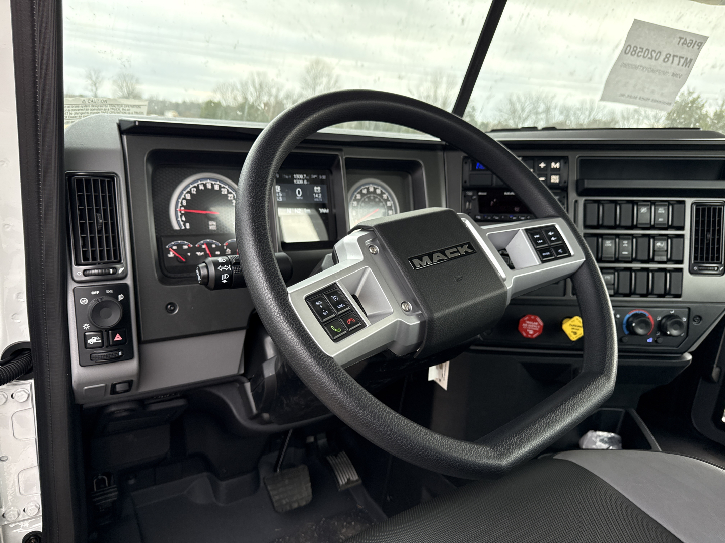 Dashboard and steering wheel of a Mack PI64T truck showing steering wheel with Mack logo, instrument cluster, and center console controls.