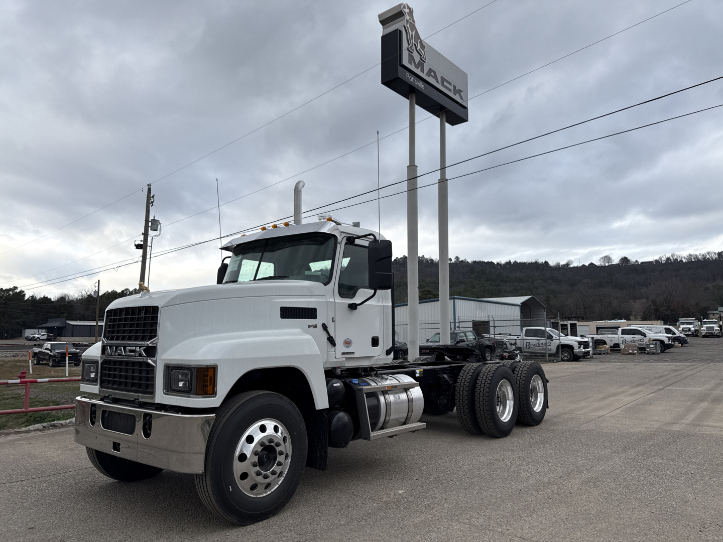 Truck chassis showing a white 2026 Mack PI64T conventional daycab from a slight front-left angle with dual rear axles and fuel tanks under the cab.