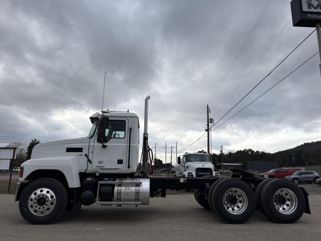 Mack PI64T truck side view showing fuel tanks and dual rear axles with chrome wheels, cab door, and vertical exhaust stack with cloudy sky.