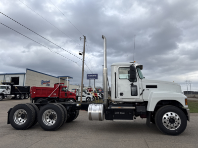 Truck side profile showing a white 2026 Mack PI64T daycab with a tall vertical exhaust stack and triple rear axles, chassis, fuel tank, and wheels visible.