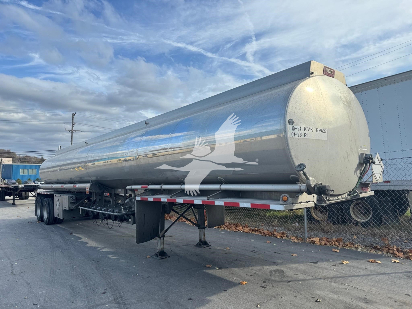 Tanker trailer showing 9200 gallon Heil with pump off line; cylindrical aluminum tank mounted on dual-axle trailer, white bird graphic on side, rear access hatch and support legs visible.