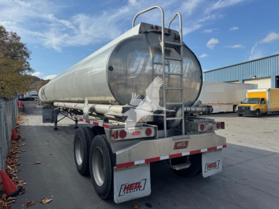 Tanker trailer showing rear and side views with twin axle, metal cylindrical tank, ladder on back, HEIL branding on mud flaps and rear bumper.