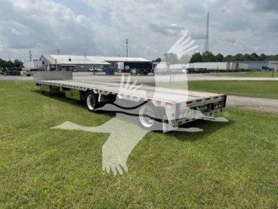 Trailer in grassy lot showing 2018 Reitnouer Dropmiser flatbed trailer with dual rear axles and fold-down deck, side rails, and rear tail lights visible.