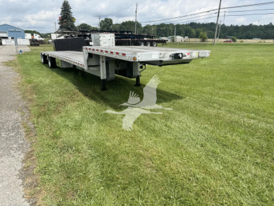 Trailer deck showing a long dropdeck trailer with dual rear ramps and multiple axles, aluminum sides, and safety markings.