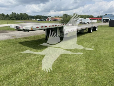 Dropdeck trailer showing flatbed with dual axles, reflective tape, and a rear loading ramp in an open lot.