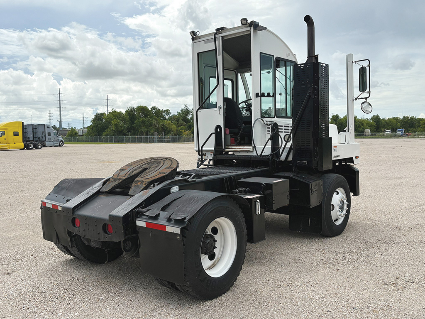 Autocar XSpotter truck with white cab, rear coupling, and large tires in a gravel lot, side view showing operator cabin and exhaust stack.