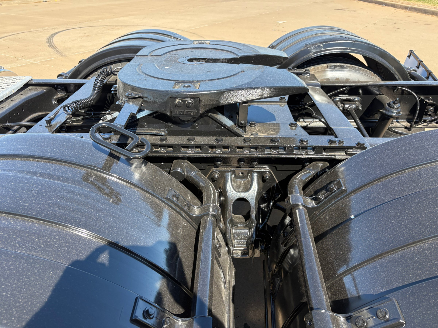 Kenworth T880 fifth wheel area showing air and power lines, frame rails, and suspension components in a close-up view.