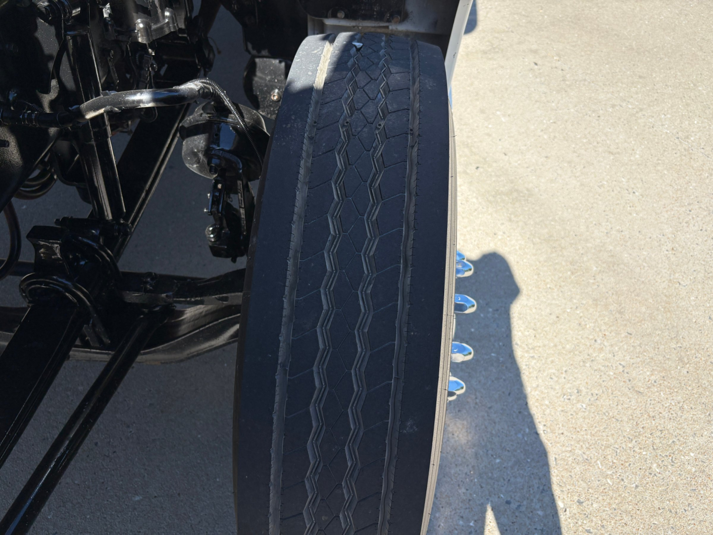 Kenworth T880 front wheel and fender area with chassis components visible; tire tread and blue fasteners along side visible.