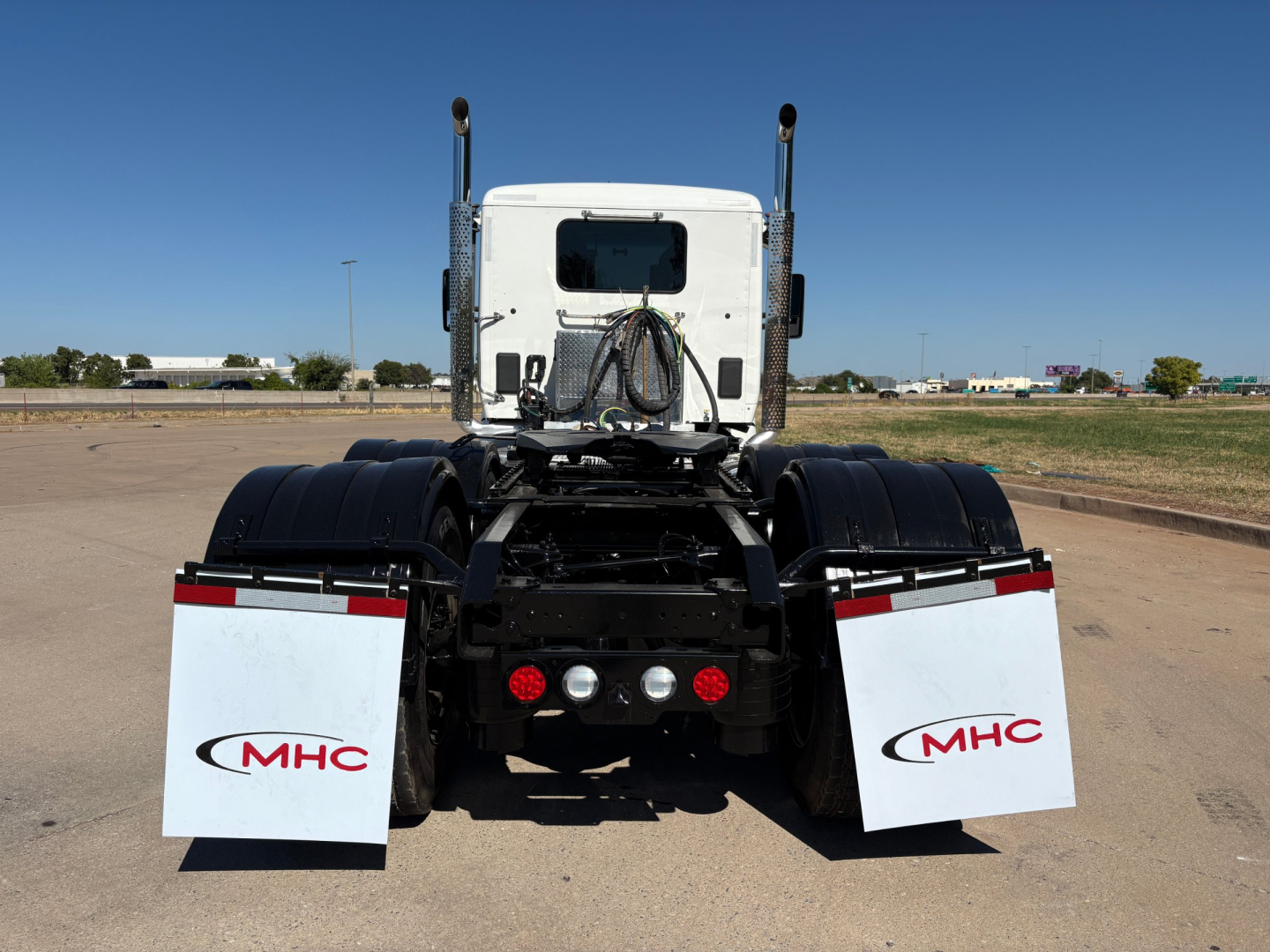 Kenworth T880 rear view showing chassis with mud flaps labeled MHC and dual exhaust stacks.