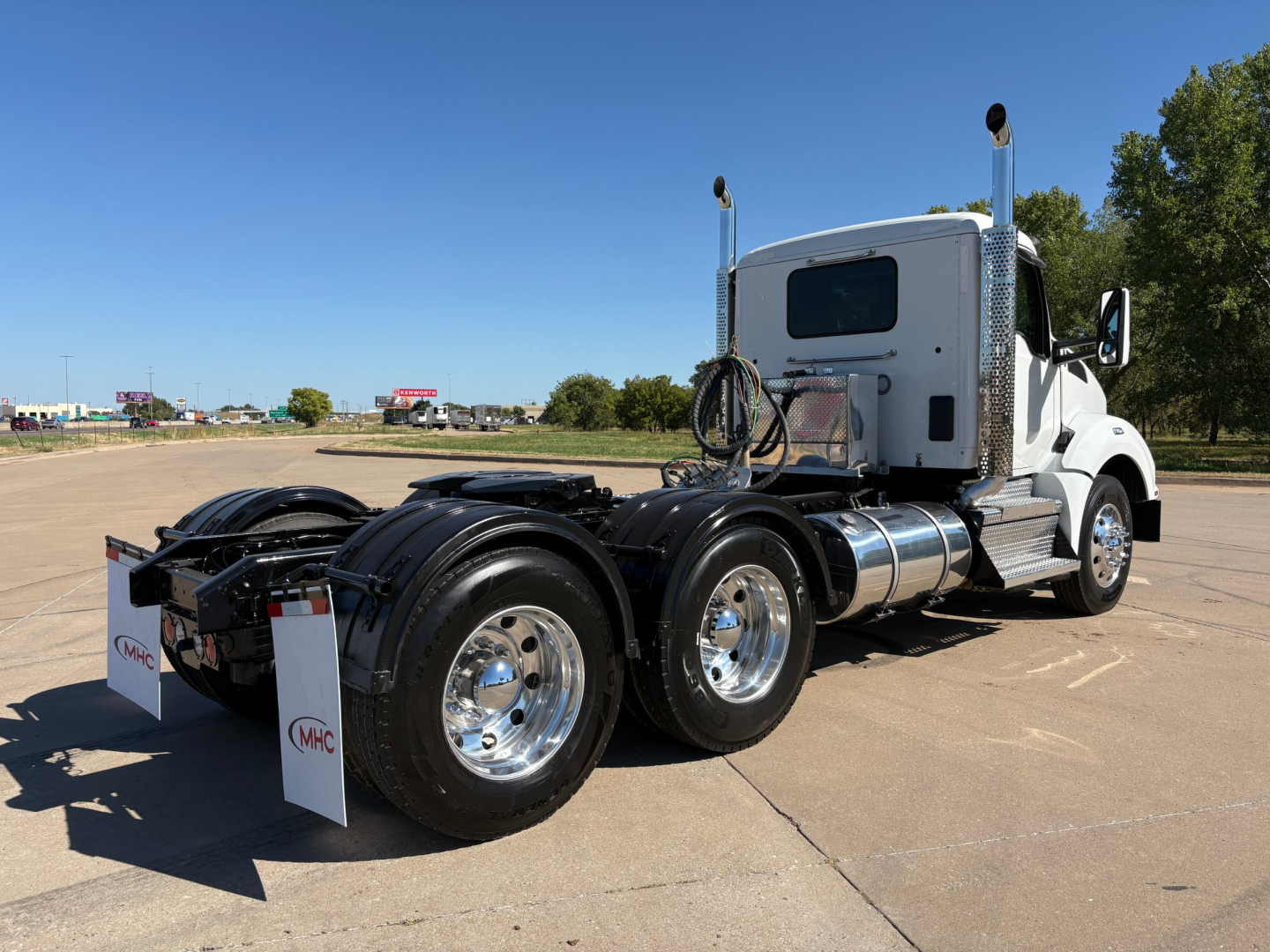 Kenworth T880 conventional daycab truck rear view showing dual rear axles and fuel tanks with chrome wheels.